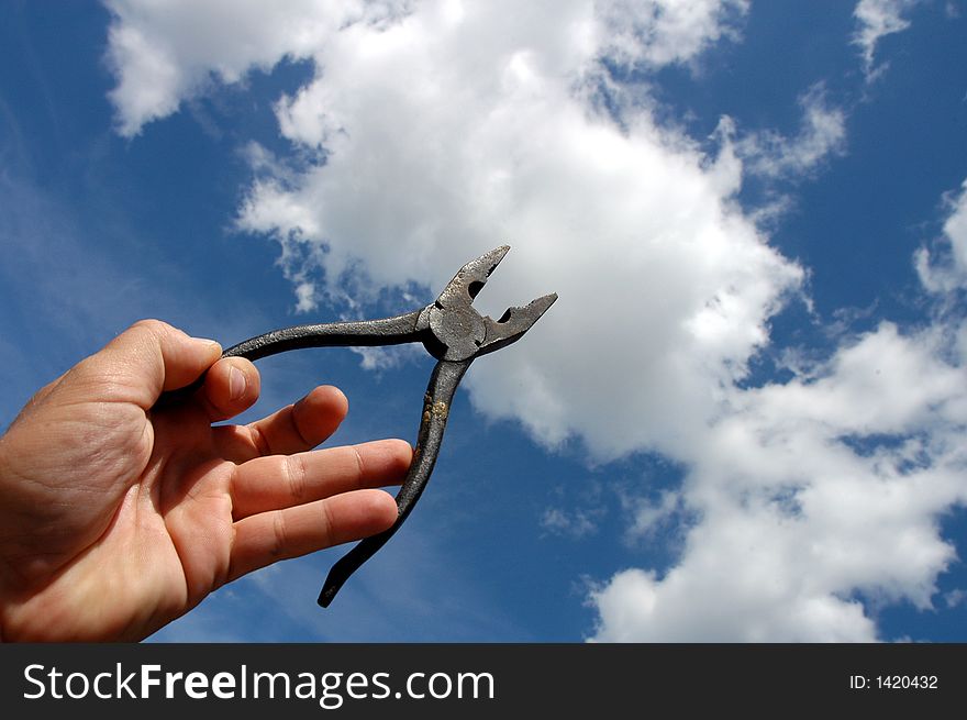 Man holding pliers against a blue sky with clouds.