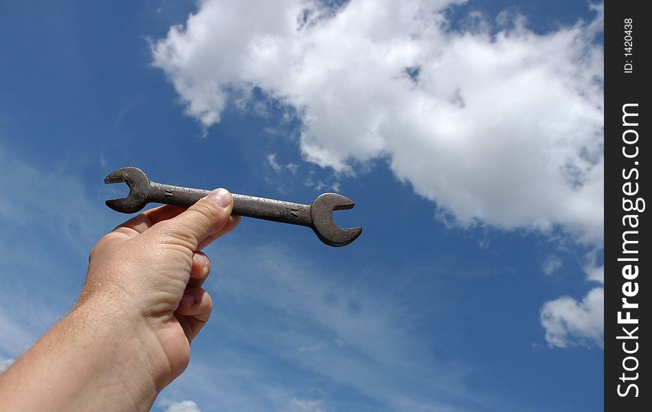 Man holding wrench against blue sky