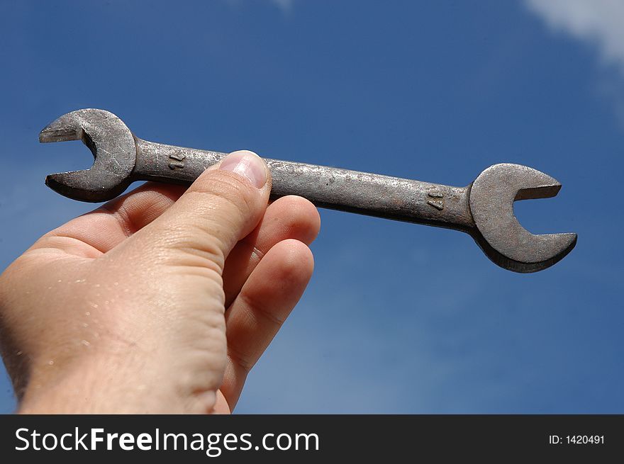 Man holding wrench against blue sky