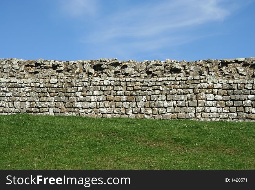 A grey stone wall divides the green grass and clear blue Sky. A grey stone wall divides the green grass and clear blue Sky