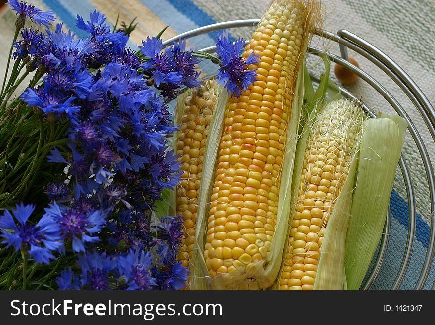 Cornflowers and grain in an iron vase on a mat. Cornflowers and grain in an iron vase on a mat