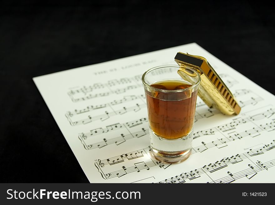 Harmonica and shot glass with whiskey on sheet music. Harmonica and shot glass with whiskey on sheet music