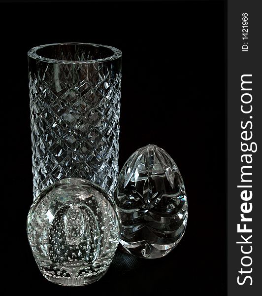 Three crystal objects, a herringbone cut vase, a suspended bubble paperweight and a cut crystal egg isolated on a black background