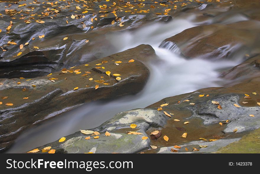 Rocks with autumn leaves and water flowing by. Rocks with autumn leaves and water flowing by