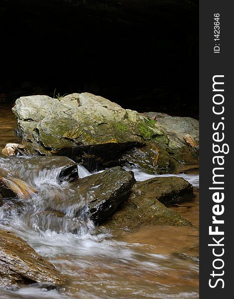 Top third of photo in deep natural shadow for copy, focus on boulder in center, waterfall pleasantly blurred through bottom half. Top third of photo in deep natural shadow for copy, focus on boulder in center, waterfall pleasantly blurred through bottom half.