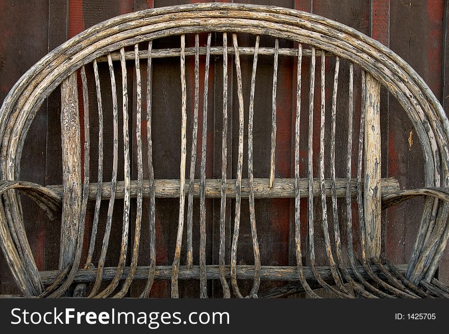 An old decaying wicker chair in front of a rustic wood building wall