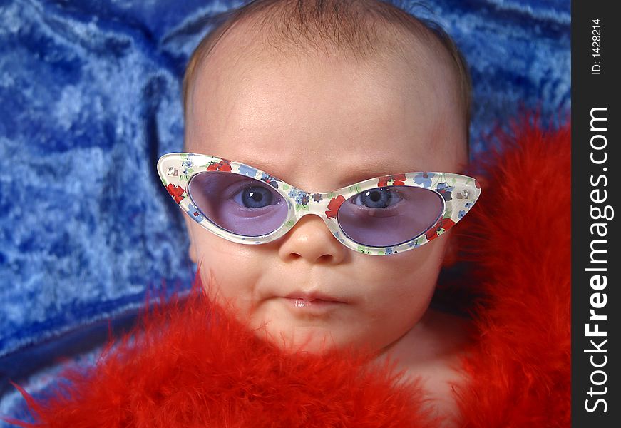 An infant girl dressed in sunglasses and a red feather boa posing for the camera. An infant girl dressed in sunglasses and a red feather boa posing for the camera