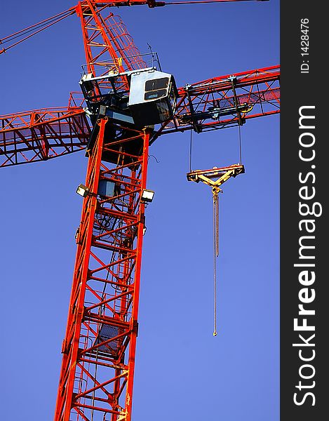 A red construction crane tower, boom, control cab, and lift point.