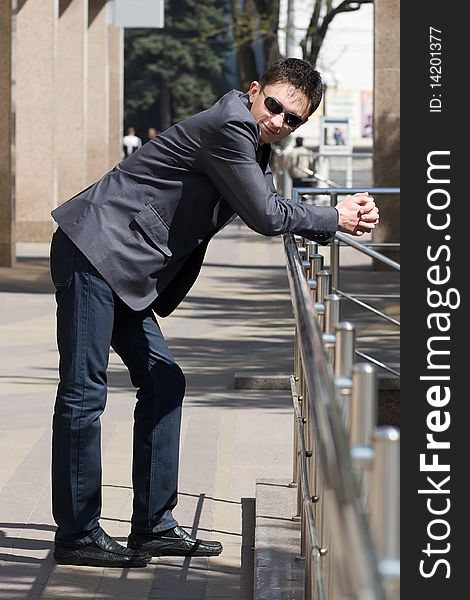 Young european businessman leans on handrails near the office building with columns smiling. Young european businessman leans on handrails near the office building with columns smiling