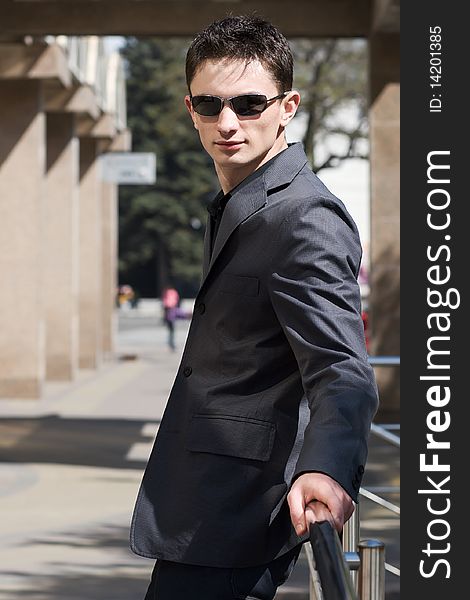 Young confident man leans on metal handrails near the office building with columns. Young confident man leans on metal handrails near the office building with columns