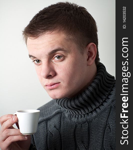 Portrait young green-eyed man in a grey sweater with a cup coffee. Portrait young green-eyed man in a grey sweater with a cup coffee