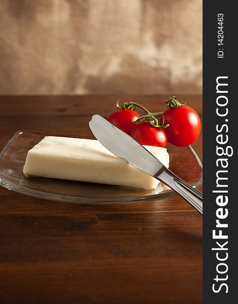 Photo of butter on a glass plate with a knife and tomatoes