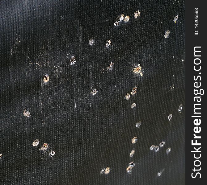 Arrow holes in black tarp practice target for archery. It also looks liek bullet holes