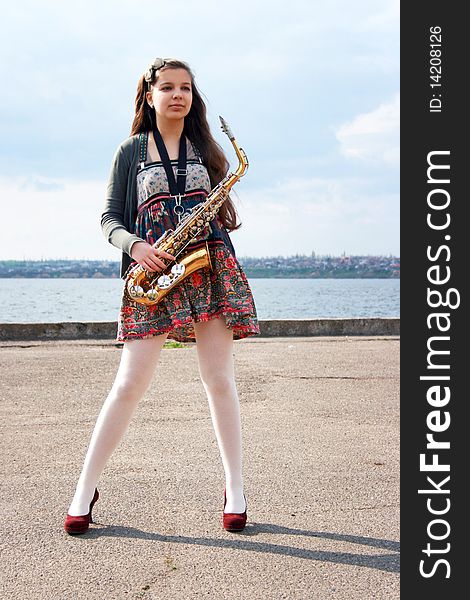 Beautiful girl with saxophone, spring beach