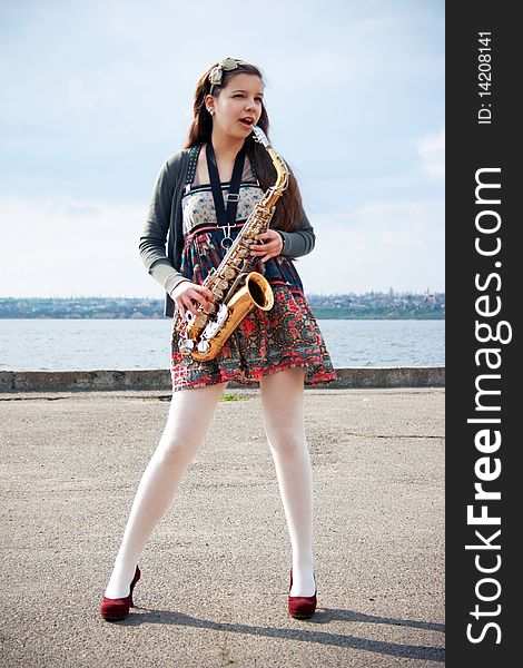 Beautiful girl with saxophone, spring beach