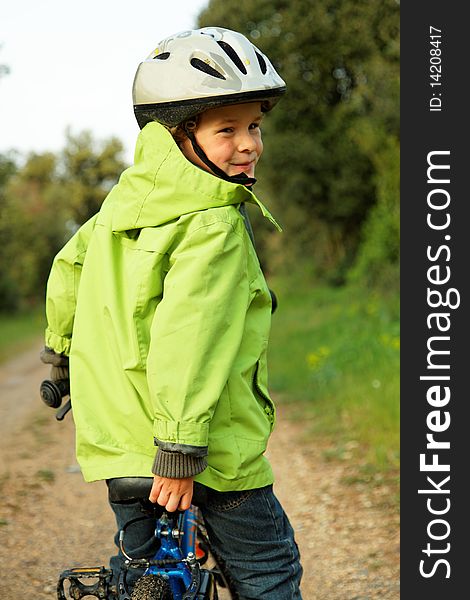 5 years old boy looking back over his shoulder while stopped on his bike, with helmet and green vest. 5 years old boy looking back over his shoulder while stopped on his bike, with helmet and green vest