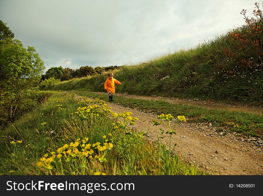 Baby girl with yellow raincoat walking along a path in the countryside, very wide framing. Baby girl with yellow raincoat walking along a path in the countryside, very wide framing