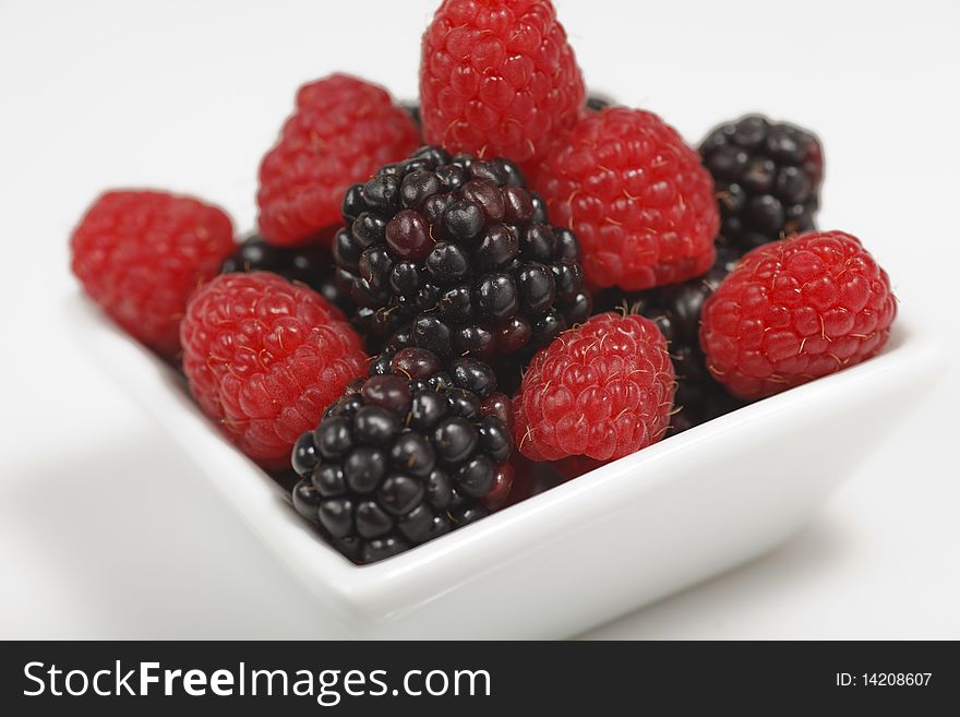Fresh raspberries and blackberries in a square dessert dish on a white background.