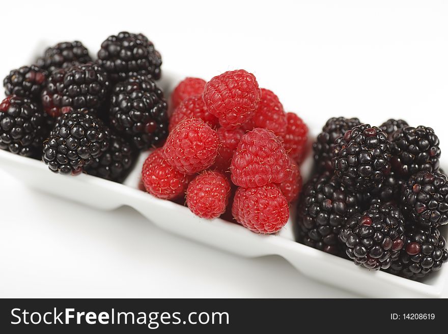 Fresh raspberries and blackberries in a rectangular dessert dish on a white background.