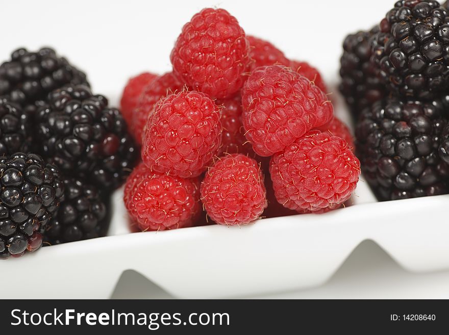 Macro image of fresh raspberries and blackberries in a rectangular dessert dish on a white background.