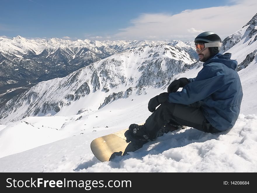 Young snowboarder in blue jacket sitting on the snow. High mountains view. Young snowboarder in blue jacket sitting on the snow. High mountains view