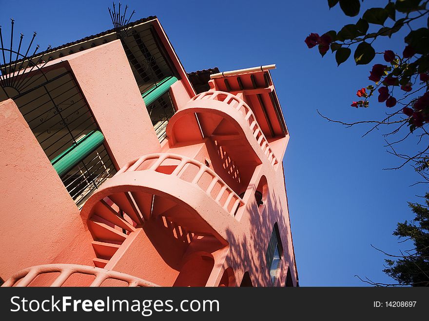 A pink hotel with spiral stairs warms in the early morning tropical light along a beach.