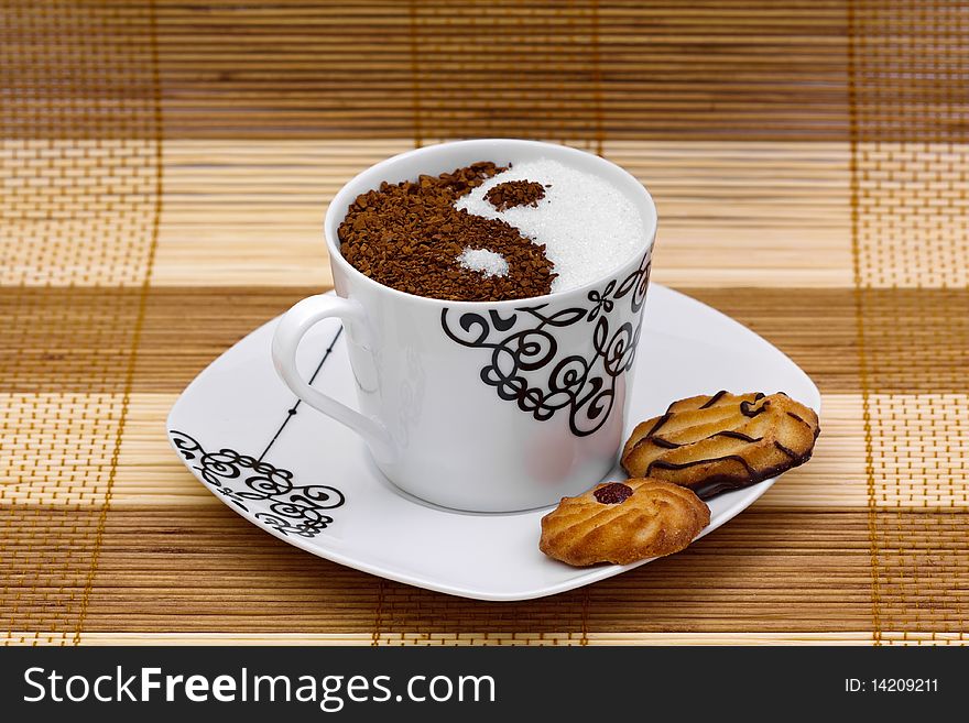 White sugar and brown coffee in a cup with the form of Yin Yang and cookies. White sugar and brown coffee in a cup with the form of Yin Yang and cookies