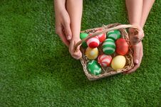 Mother And Her Little Child With Basket Of Painted Easter Eggs On Green Grass, Top View. Stock Photo