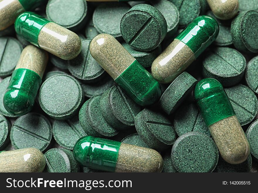 Green spirulina pills and capsules as background, closeup