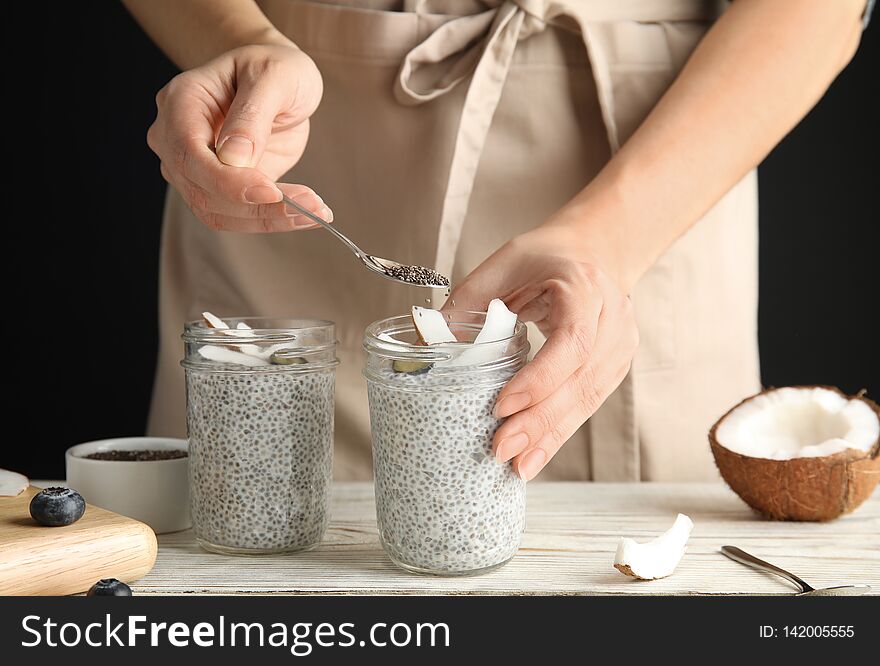 Young woman preparing chia seed pudding with coconut at table