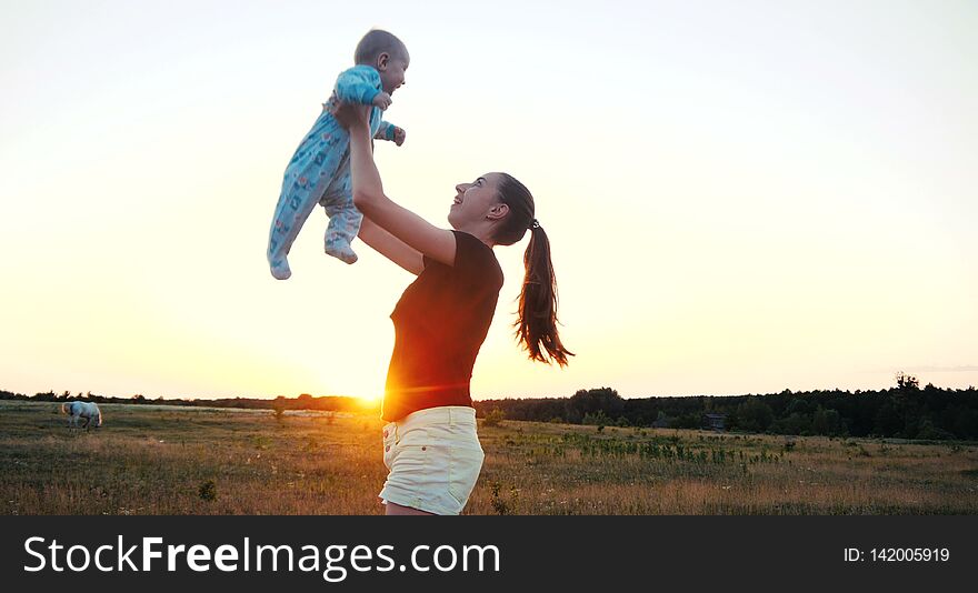 Emotional young woman raising her baby in hands in a field at sunset in slo-mo