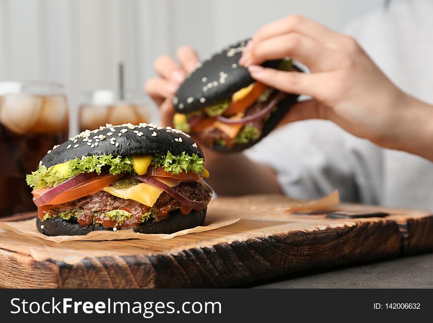 Tasty burger with black buns and woman eating