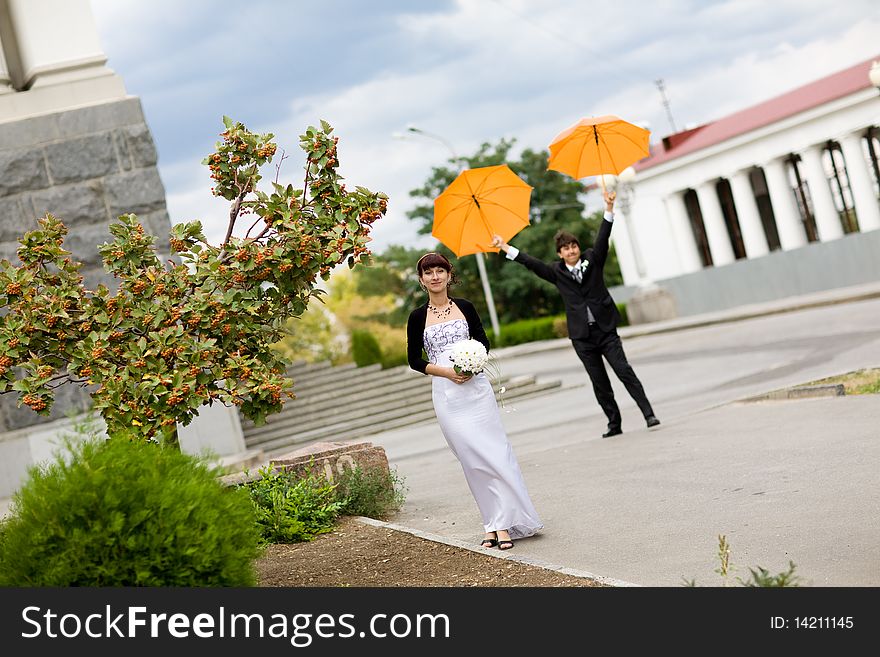 Laughing  bride and groom with orange umbrellas