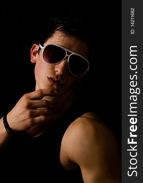 Young fashion guy with athletic body posing in sun glasses, on black background