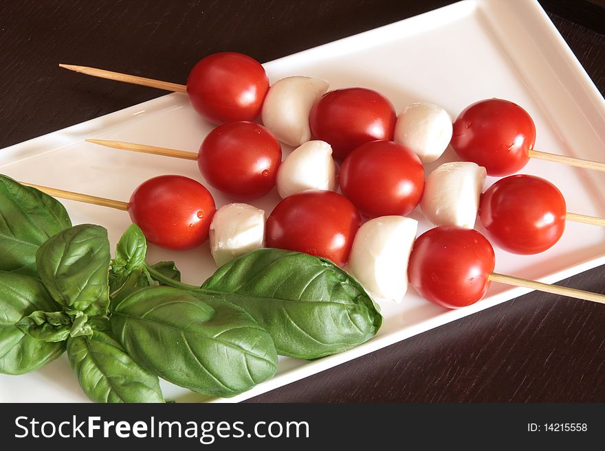 Vegetarian kebab of cherry tomatoes and mozzarella on skewers in a white dish, black background