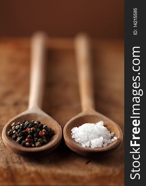 Salt and pepper grains on wooden spoon on a old wooden table