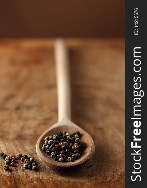 Colorful pepper on a wooden spoon over a wooden table