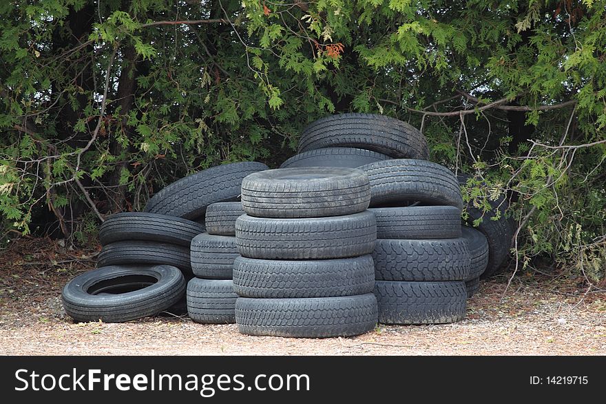 A stack of used old tires sit in a yard along a hedgerow showing recyling issues. A stack of used old tires sit in a yard along a hedgerow showing recyling issues.