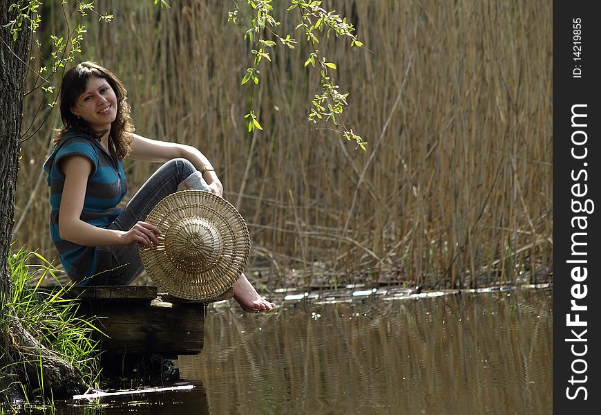 Girl in straw hat sitting near lake shore. Girl in straw hat sitting near lake shore