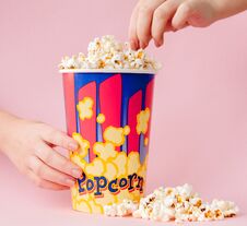 Free Hand Takes A Popcorn From A Paper Cup On A Pink Background. Woman Eats Popcorn.Cinema Concept. Flat Lay. Copyspace Royalty Free Stock Photography - 142134987