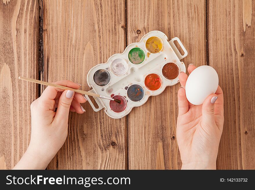 Close-up of woman`s hands painting an easter egg on wooden background