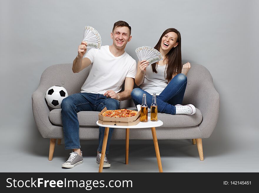 Cheerful couple woman man football fans cheer up support favorite team holding fan of money in dollar banknotes, cash