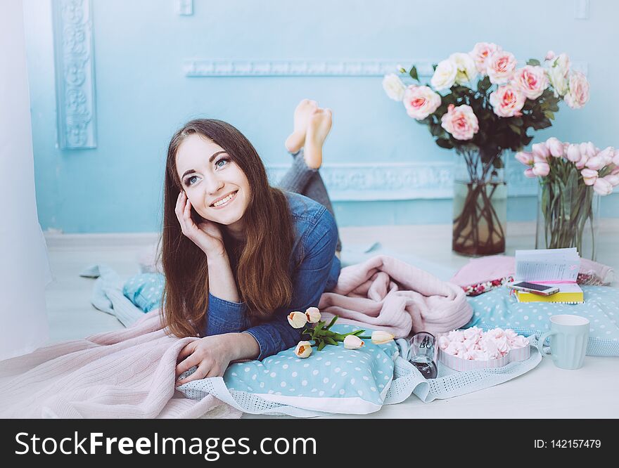 Beautiful girl lying on the floor and smiling, with tulip flowers on the blue wall background in the spring morning.