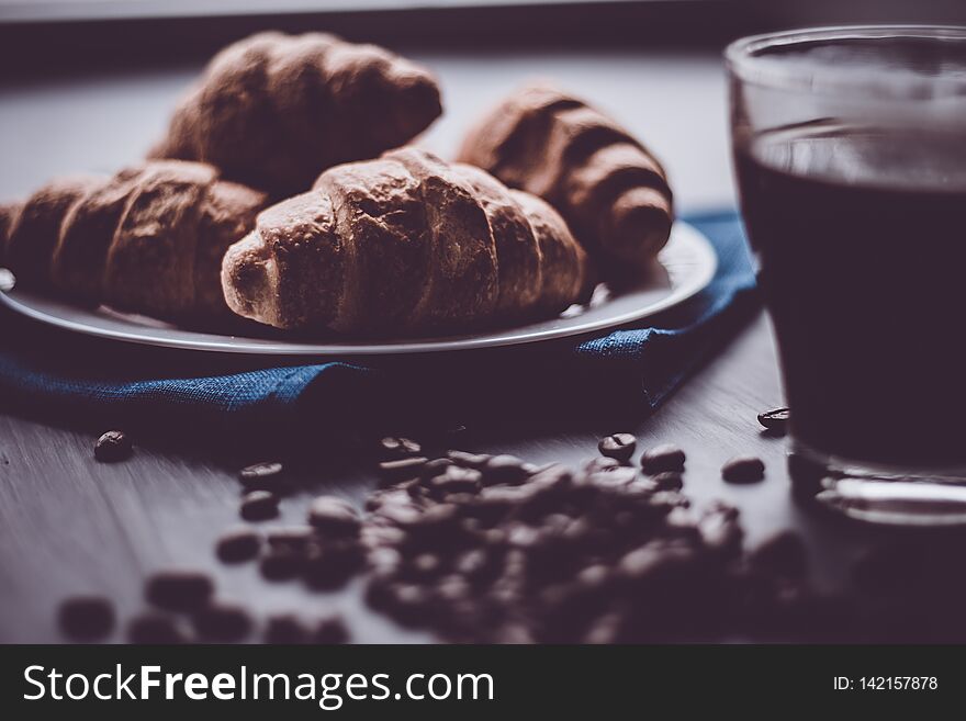 The concept of breakfast. Dessert and coffee beans. Mate moody color. Macro shot of fresh croissants and coffee on a black background.