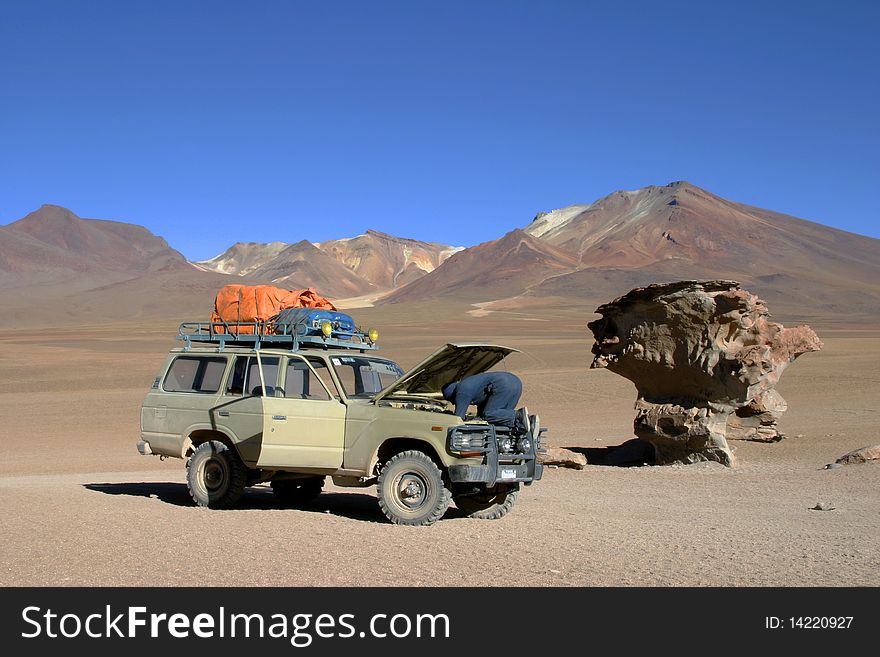 Man repairing car in the Bolivian desert beseide the famous Arbol de Piedra. Man repairing car in the Bolivian desert beseide the famous Arbol de Piedra