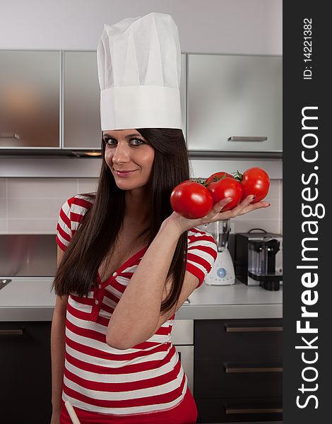 Lovely girl wearing cook cap and holding tomatoes in kitchen.