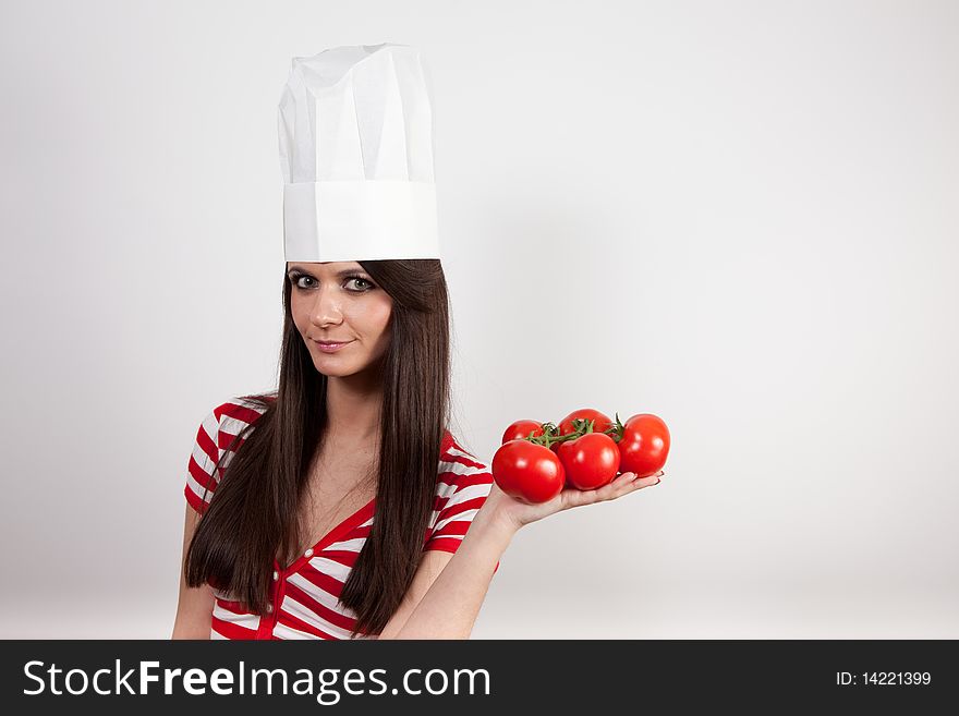 Lovely girl wearing cook cap and holding tomatoes, isolated on white.