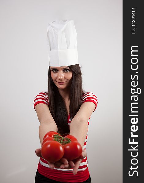 Lovely girl wearing cook cap and holding tomatoes, isolated on white.