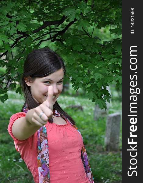 Young beautiful girl holding a thumb up in a background of nature. Young beautiful girl holding a thumb up in a background of nature