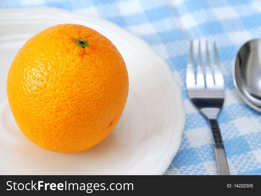 Closeup of orange on plate with utensils. Healthy eating and lifestyle, diet and nutrition, and fresh fruit concepts . Closeup of orange on plate with utensils. Healthy eating and lifestyle, diet and nutrition, and fresh fruit concepts .